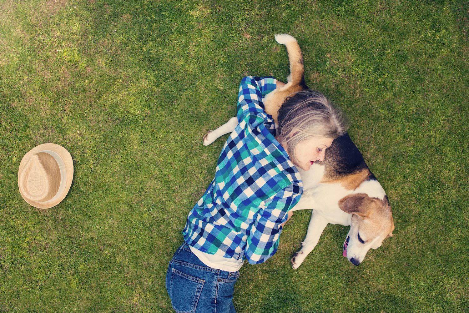 A mature woman resting with her dog on the grass outdoors.
