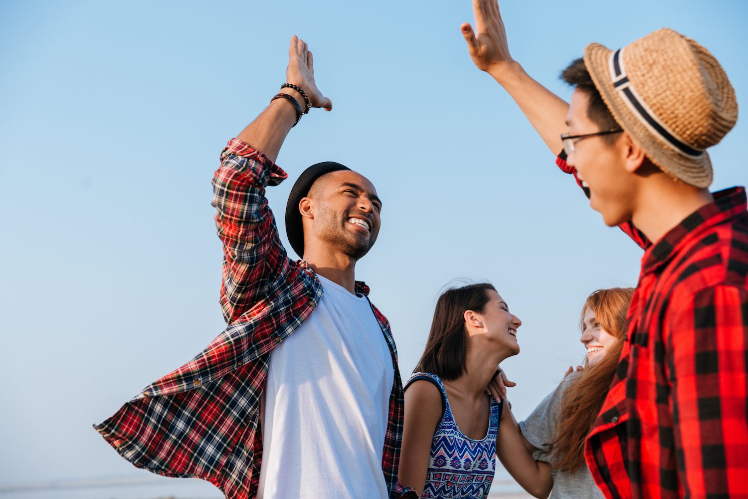 Cheerful young friends laughing and giving high five outdoors.