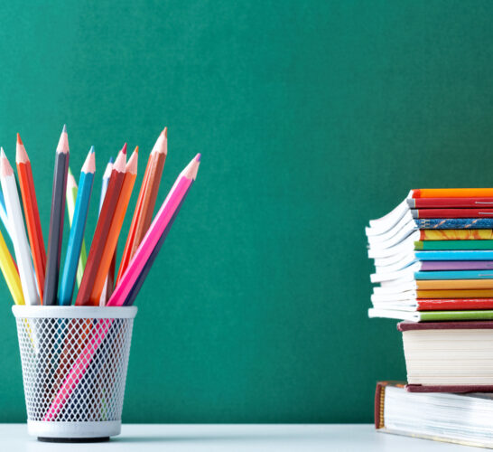 Image of colored pencils in a cup and a stack of books against a green chalkboard.