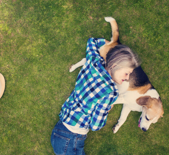 A mature woman resting with her dog on the grass outdoors.