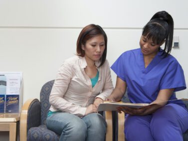 Patient in a medical setting sitting with a nurse.
