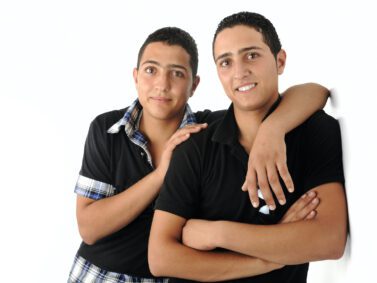 Two young male friends leaning against a wall supporting one another.